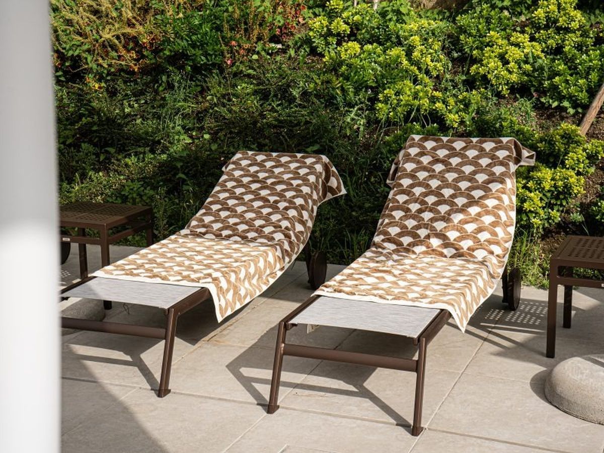 Due poltrone con cuscini decorati su un patio con pavimento piastrellato, immerso nel verde.