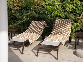 Dos sillones de relax con cojines estampados en un patio con suelo de baldosas, rodeado de follaje.