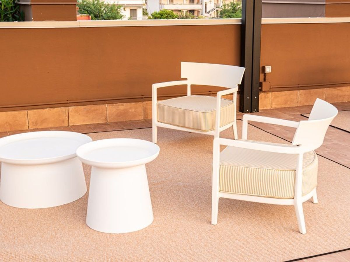 Un patio con dos sillas y dos mesas blancas.