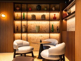 Un interior moderno con dos sillones de cuero, una mesa redonda y un estante de pared con diversos objetos decorativos.