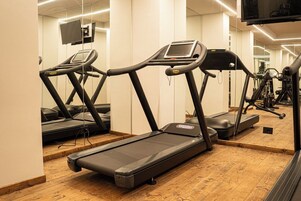 Un gimnasio con varias cintas de correr, un televisor montado en la pared y piso de madera.
