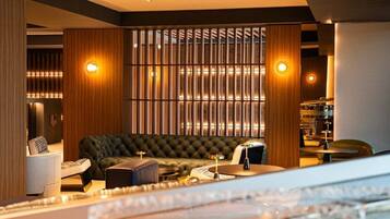Un interno moderno con un divano trapuntato, un pannello divisorio in legno con listelli verticali e un angolo bar con sgabelli.