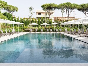 A rectangular swimming pool with lounge chairs and umbrellas, surrounded by greenery and buildings in the background. - Grimaldi Boutique Hotel (Lago Patria)