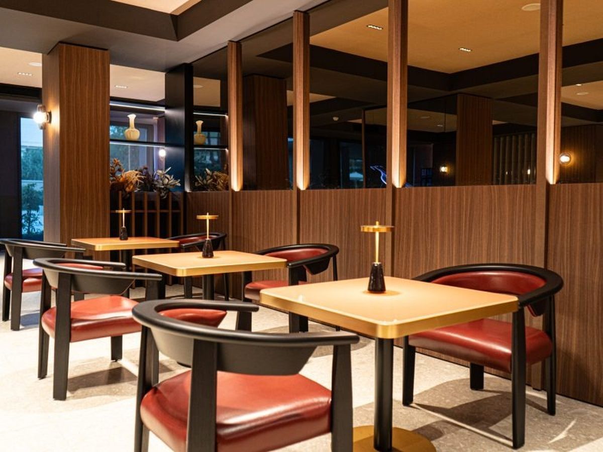Interior de restaurante con paneles de madera, varias mesas y sillas tapizadas rojas.