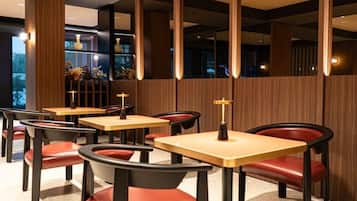 Interior de restaurante con paneles de madera, varias mesas y sillas tapizadas rojas.