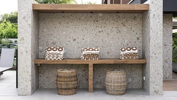 Un banc en béton, avec des paniers tressés placés en dessous, adossé à un mur de pierre.