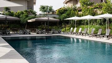 Une piscine entourée de verdure et de bâtiments, avec des chaises longues et des parasols.