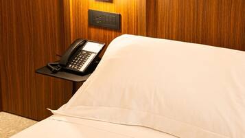 Una camera d'albergo con un letto, un telefono sul comodino e un punto luce a parete.