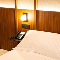 Una habitación de hotel con una cama, un teléfono en la mesita de noche y una lámpara fijada a la pared.