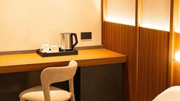 Una camera d'albergo con una scrivania in legno, una sedia, un letto e una lampada a muro.