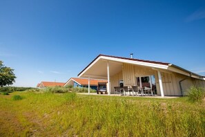A single-story building with a covered patio area, featuring a table and chairs. - "P-Liner" house type E plus (Neustadt\/Holstein - OT Pelzerhaken)