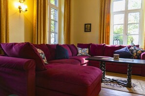 A room with a large red sofa set, a small table, and a window with curtains. - Manor House Kleine Gönn (Xanten)
