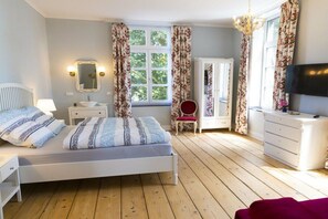 A bedroom with a bed, bedside tables, a mirror, a dresser, and a television. - Manor House Kleine Gönn (Xanten)