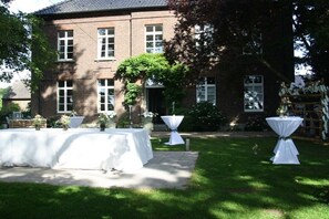 A brick building with a garden patio area featuring tables set for an event. - Manor House Kleine Gönn (Xanten)