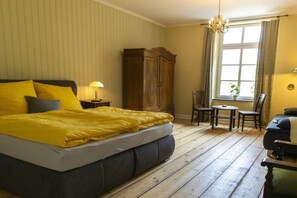 Een slaapkamer met een groot bed, een kledingkast, een klein tafeltje en een stoel.