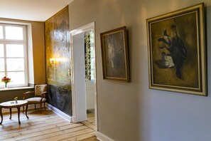 A room with a wooden floor, a chair, a table, and two framed artworks on the wall. - Manor House Kleine Gönn (Xanten)