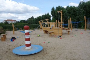 Ein Spielplatz mit Sandkasten, Klettergerüsten und einer Hängebrücke.