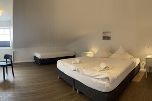 Ein Schlafzimmer mit einem großen Bett, einem kleineren Bett, einem Sessel und einem Nachttisch mit einer Lampe.