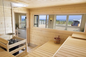 Ein Holzinnenraum mit Sauna, Meerblick und einer Holzterrasse außen.