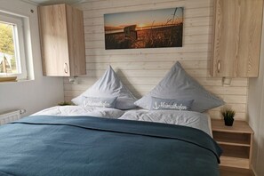 Ein Schlafzimmer mit Bett, Kissen, einem Nachttisch, einem Fenster und einem Wandbild.