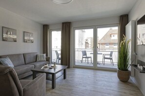 A modern living room with a sofa, coffee table, and a large window with curtains. - Holiday apartment with 1 bedroom (Cuxhaven)