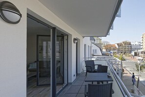 Un balcó amb taula i cadires, una porta corredissa de vidre i vista al carrer i edificis.