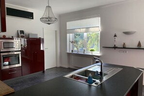 A modern kitchen with a built-in oven, a stainless steel sink, and a window with a view of greenery. - Apartment by the sea (Travemünde)