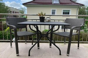 A balcony with a table and two wicker chairs, a potted plant, and a vase. - Apartment by the sea (Travemünde)
