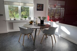 A dining area with a round table, four chairs, a vase with flowers, and a window with plants. - Apartment by the sea (Travemünde)