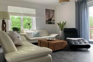 A modern living room with a sofa, a black ottoman, a coffee table, and a fireplace. - Apartment by the sea (Travemünde)