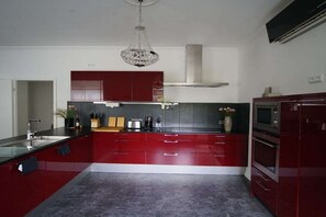 A modern kitchen with red cabinetry, a stainless steel range hood, and a chandelier. - Apartment by the sea (Travemünde)