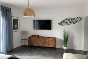 A modern living room with a flat-screen TV mounted on the wall, a wooden console table, a floor lamp, and a large potted plant. - Apartment by the sea (Travemünde)