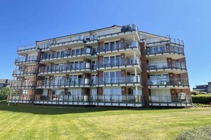 A multi-story residential building with balconies, a flat roof, and a grassy front yard. - Strandpalais Apt. C1 (Cuxhaven)