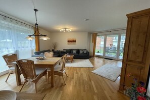 A spacious living room with a wooden dining table, chairs, a sofa, and a chandelier. - Strandpalais Apt. C1 (Cuxhaven)