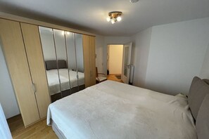 A bedroom with a bed, a wardrobe, a mirror, and a ceiling light fixture. - Strandpalais Apt. C1 (Cuxhaven)