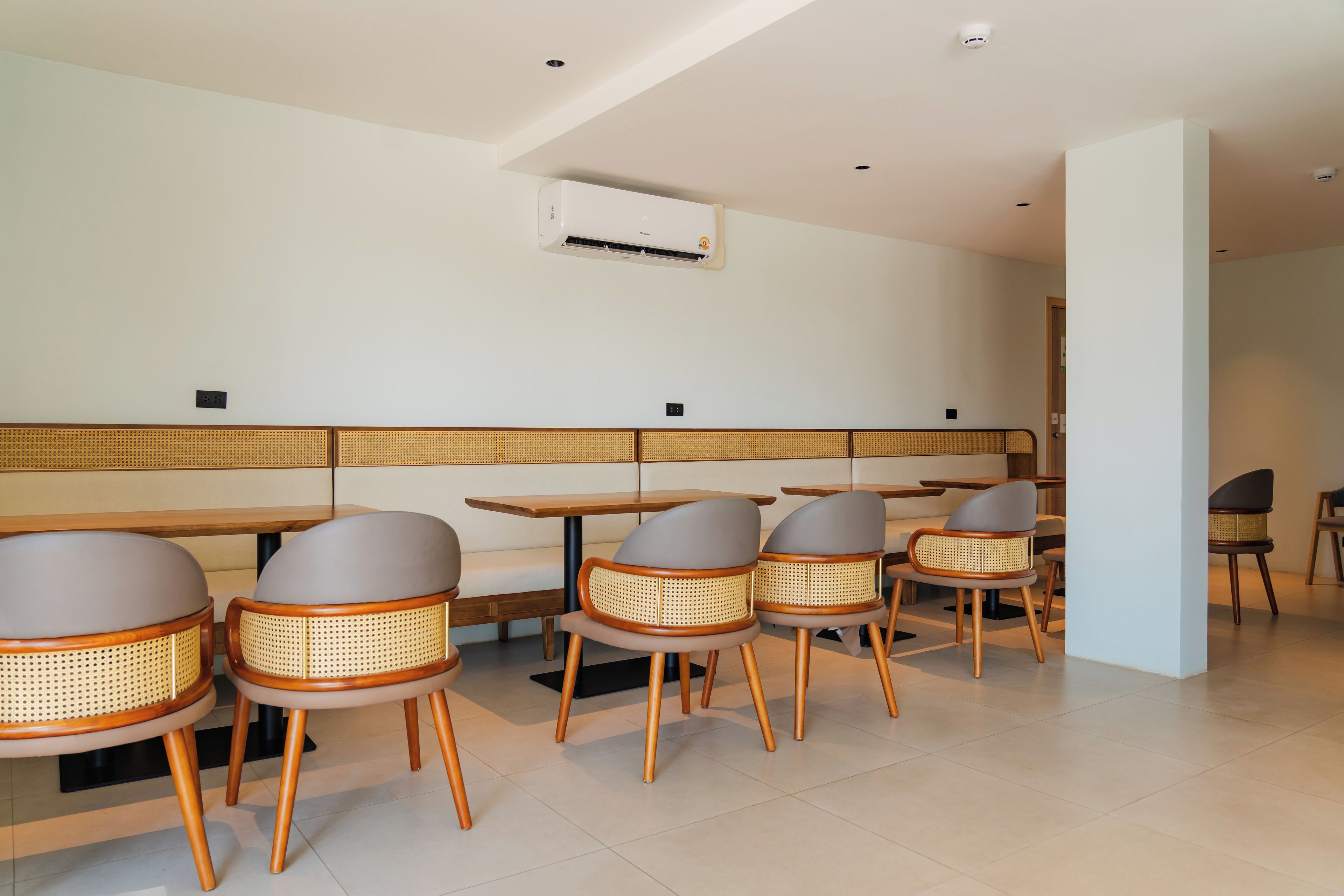 Un espace repas moderne avec des tables en bois et des chaises en rotin, un plafond blanc et un appareil de climatisation.