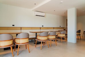 A modern dining area with wooden tables and rattan chairs, a white ceiling, and an air conditioning unit. - Brand-New Luxury Condo with Ultimate Convenience (Koh Samui)