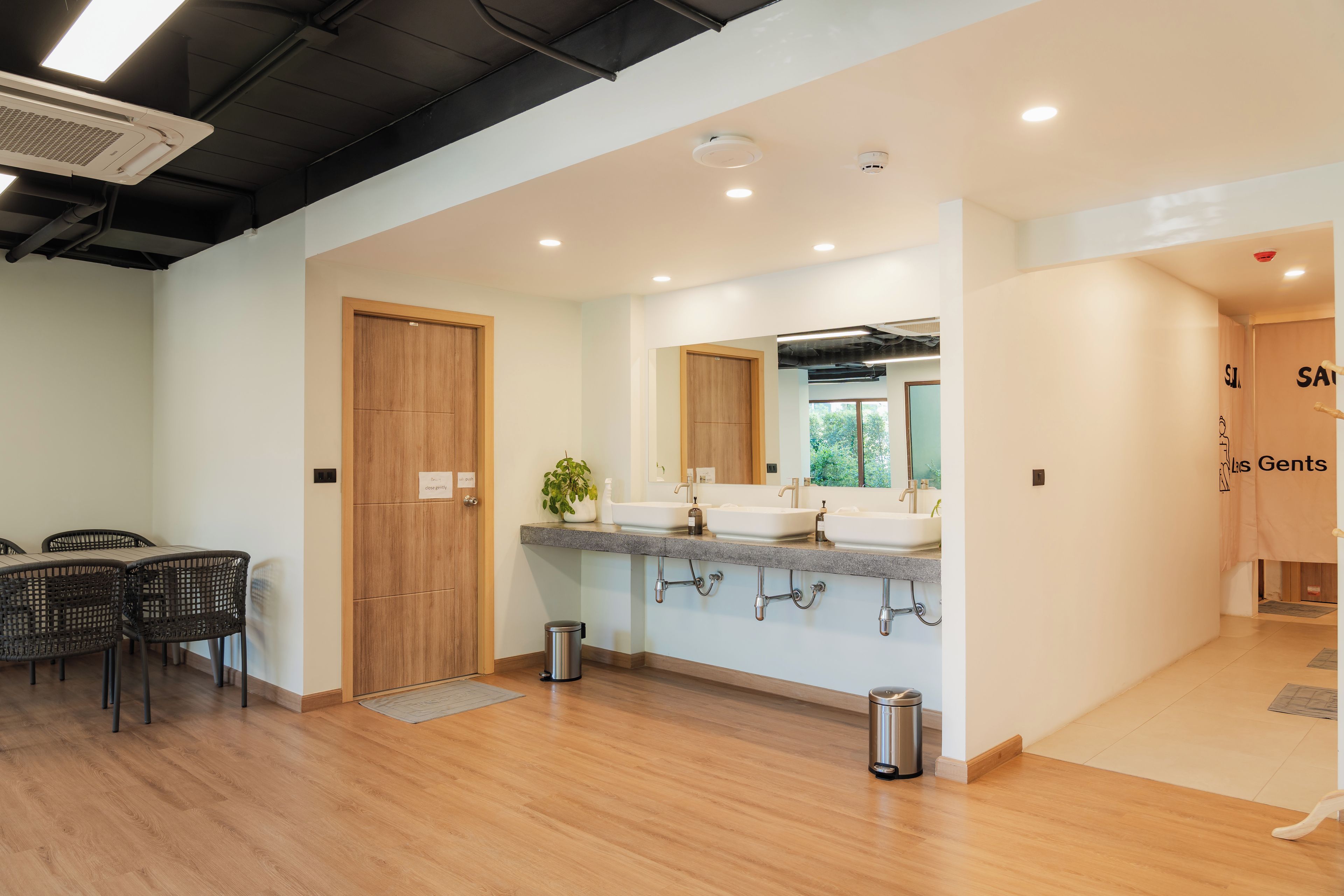 A modern bathroom with a wooden door, a sink with a mirror, and a trash bin.