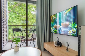 Un salon moderne avec un grand téléviseur à écran plat fixé au mur, une table à manger ronde entourée de chaises, une plante en pot et un meuble en bois agrémenté d’objets décoratifs.