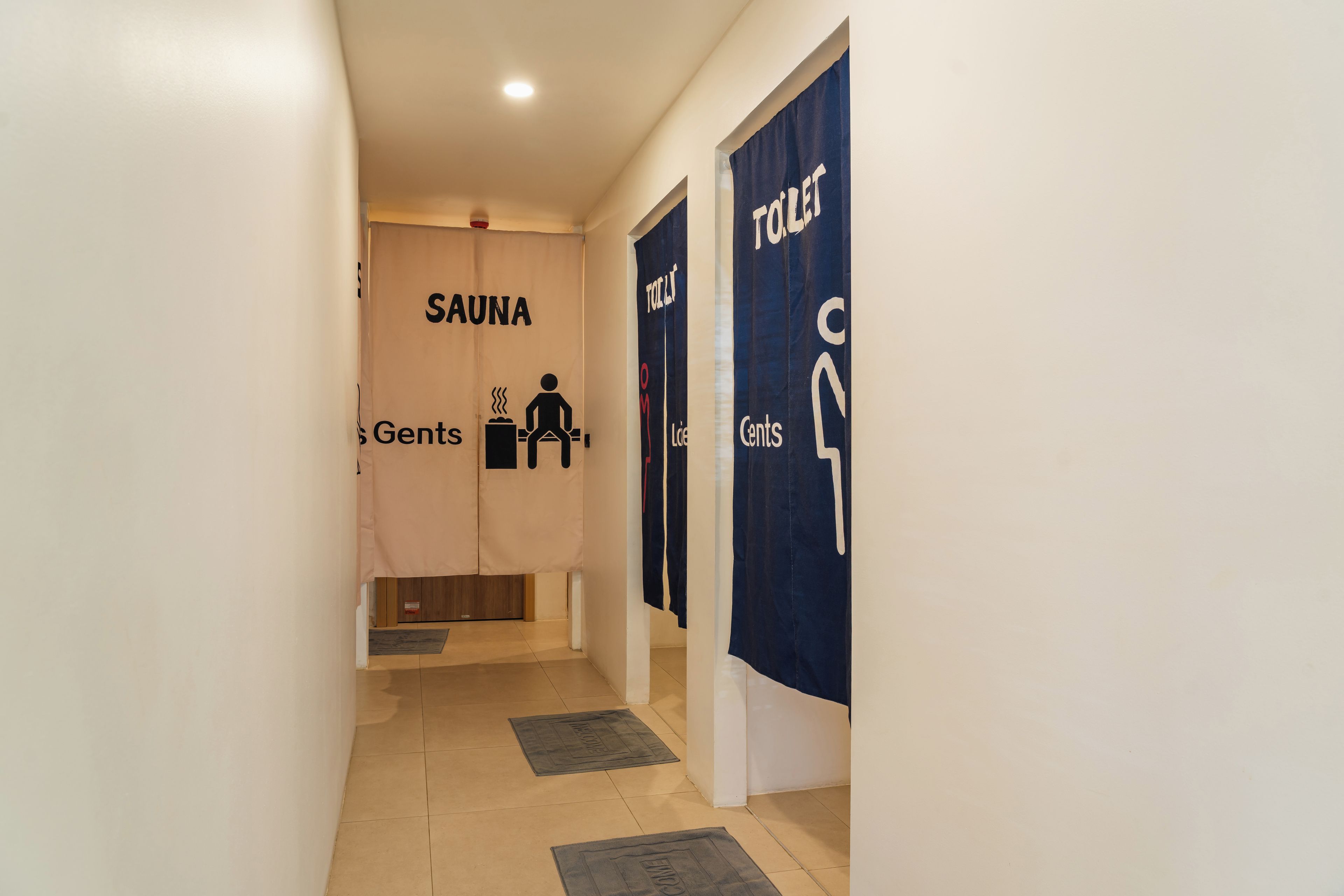Un couloir donnant accès à un espace sauna et à des toilettes pour hommes.