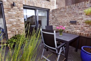 Une terrasse extérieure avec une table et des chaises, une plante en pot et un mur en briques.