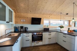 A modern kitchen with a wooden ceiling, built-in cabinets, a stainless steel oven, and a coffee maker. - "Shipping House" Type G plus (Neustadt\/Holstein - OT Pelzerhaken)