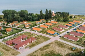 A residential area with multiple houses, a central building with a red roof, and a body of water in the background. - "Shipping House" Type G plus (Neustadt\/Holstein - OT Pelzerhaken)