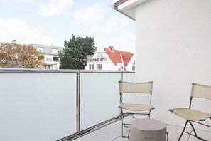 A balcony with two chairs and a round table, overlooking a residential area with houses and trees. - Timmare III Penthouse (Timmendorfer Strand)