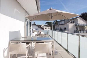 A balcony with a glass railing, a table, chairs, and an umbrella. - Timmare III Penthouse (Timmendorfer Strand)