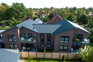 Une maison à deux étages, construite en briques, avec un toit en pente, un balcon à l’étage supérieur et une cour arrière clôturée.