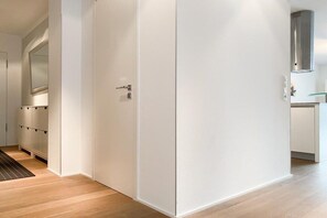 Ein Flur mit einem weißen Kleiderschrank, einer Tür mit Griff und einem Küchenbereich mit einer Glastür.