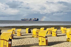 A beach with rows of yellow beach chairs and a cargo ship in the background. - Holiday apartment Duhner Allee 10 "Sünnsied" (Cuxhaven)