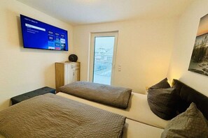 Ein Zimmer mit zwei Betten, einem an der Wand montierten Fernseher, einer Tür und einem Fenster.