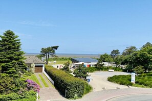 Ein Wohngebiet mit befestigter Auffahrt, einem kleinen Gebäude mit geneigtem Dach und Blick auf das Meer im Hintergrund.